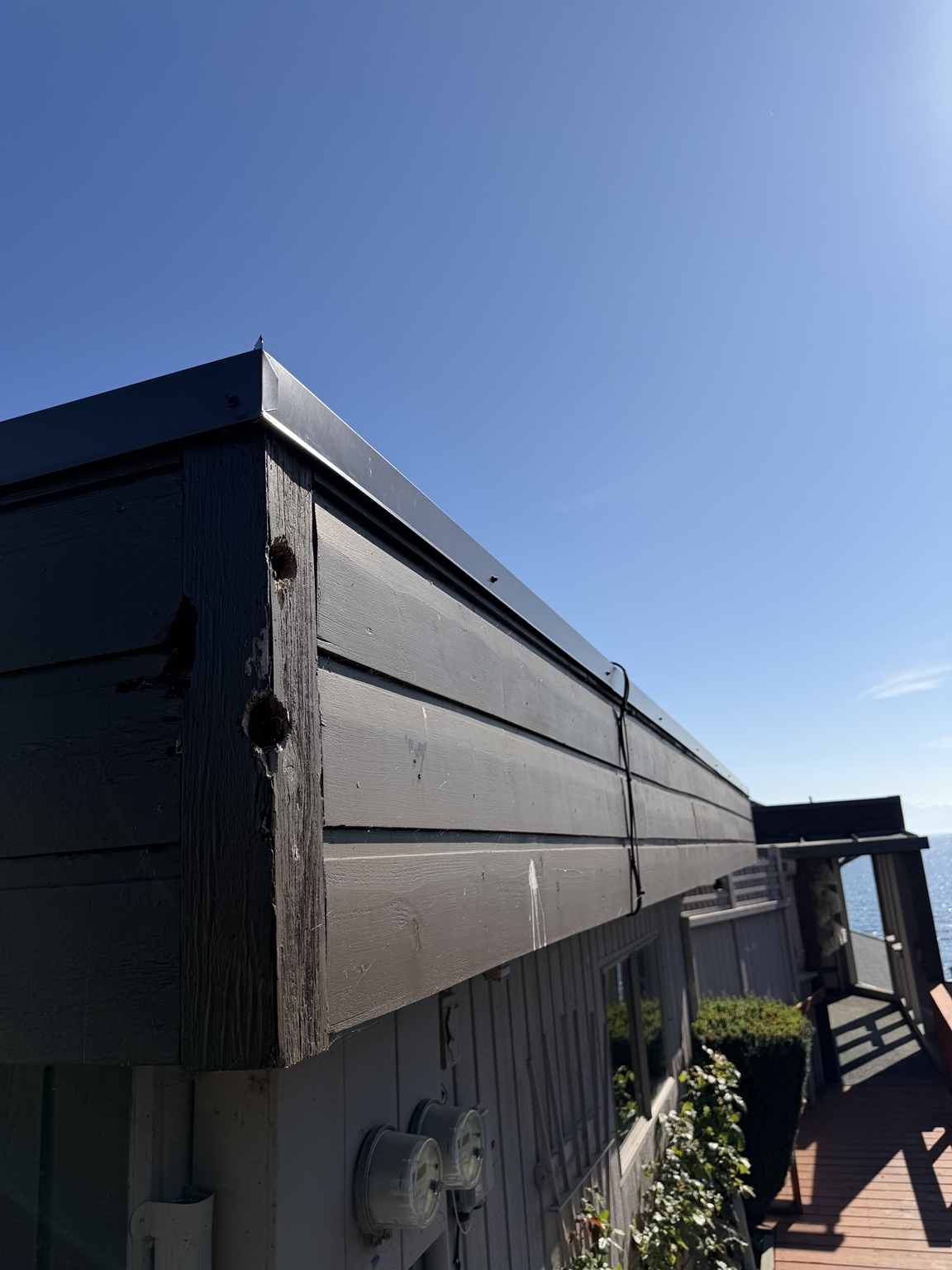 Corner of a flat roof with dark wood fascia and black metal cap flashing