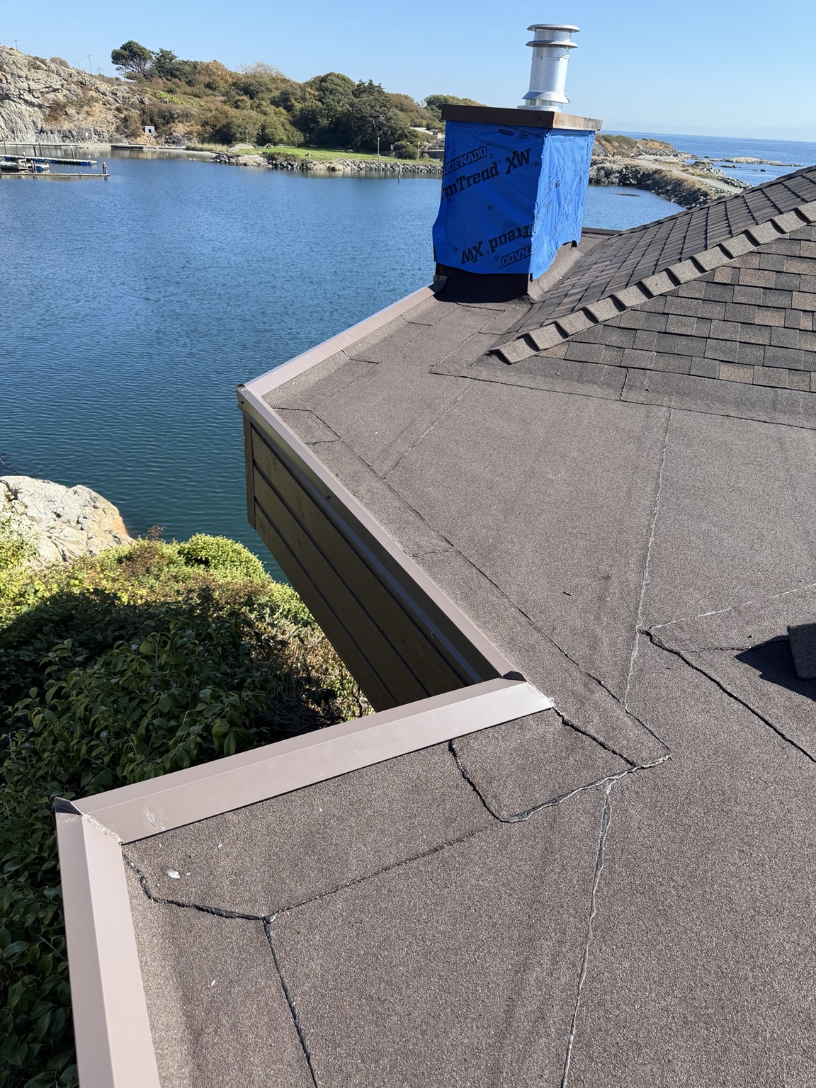 Metal edge flashing along a flat roof meeting a shingled roof slope