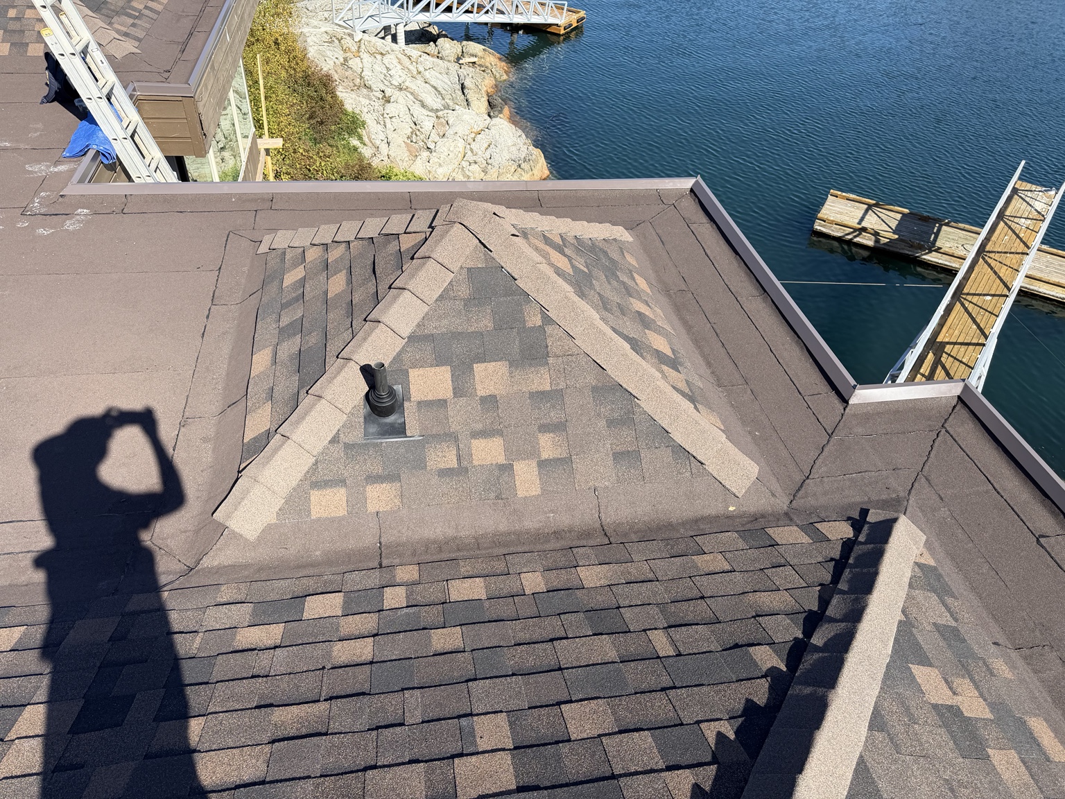 Low-slope roof with granulated membrane and metal drip edge beside shingled hip roofs