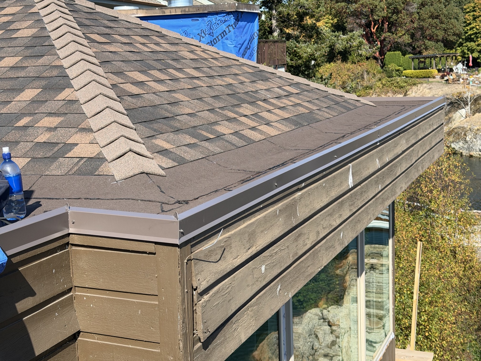 Close view of a shingled hip ridge meeting a low-slope roof edge with metal drip edge above wood siding