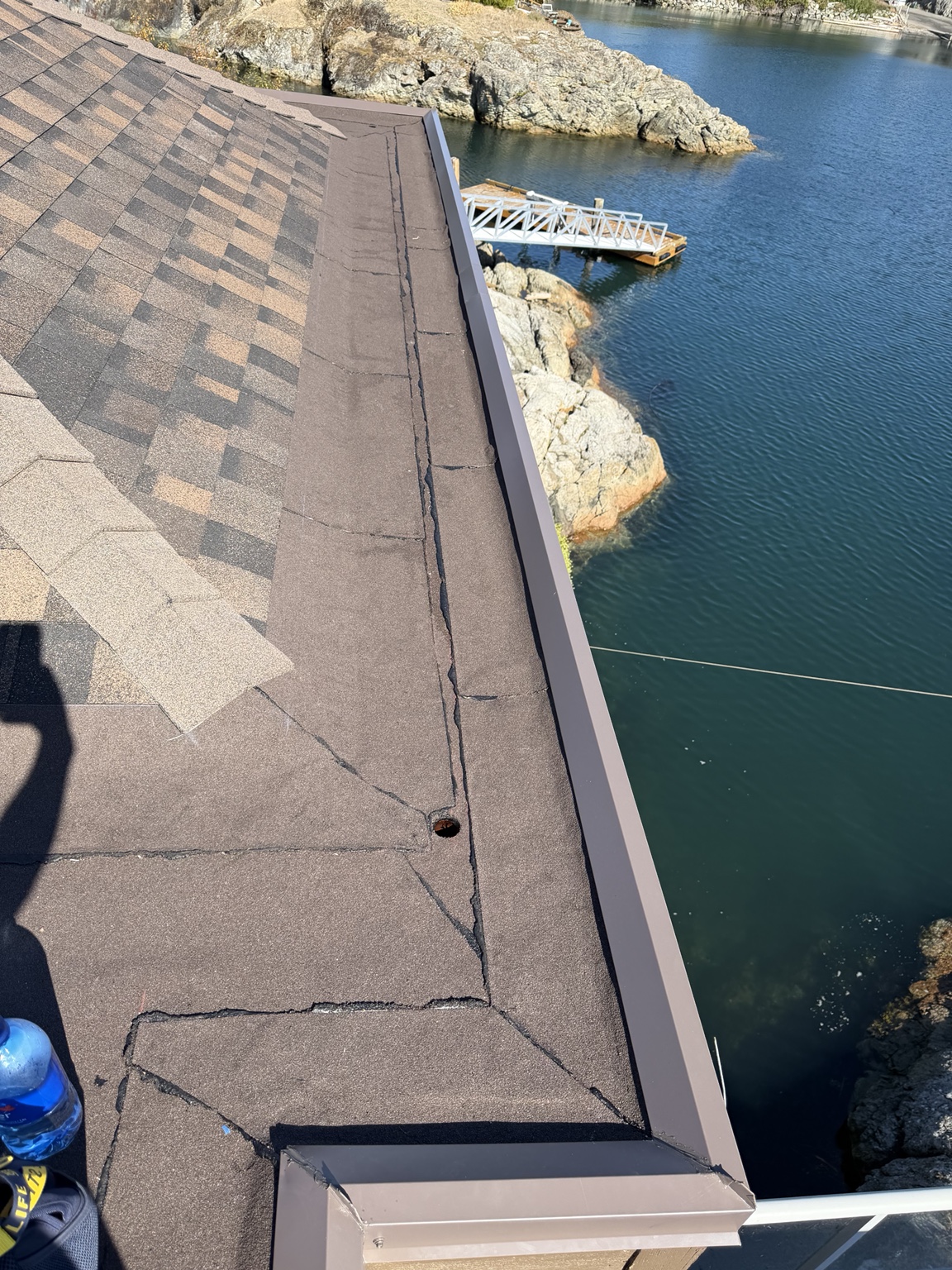Granulated membrane roof surface with seam sealant and a drain, edged with metal flashing beside a shingled slope