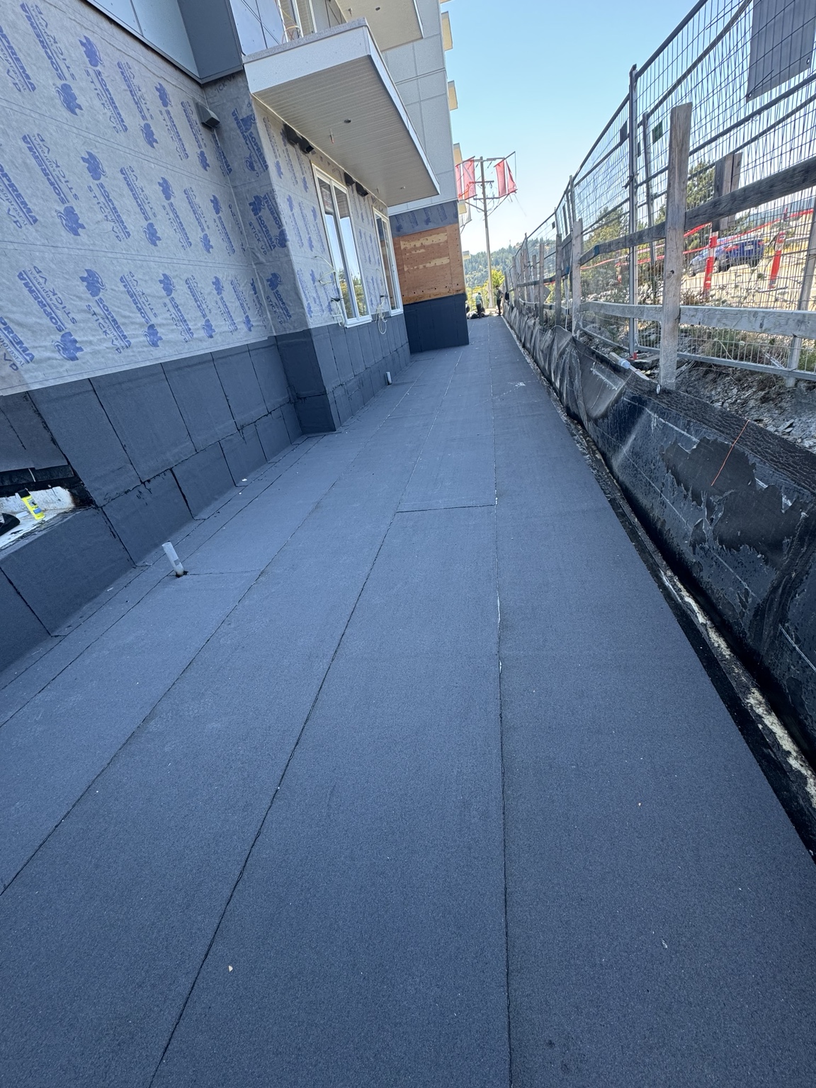 Long membrane surface with wall upstands along a fenced edge of a building under construction