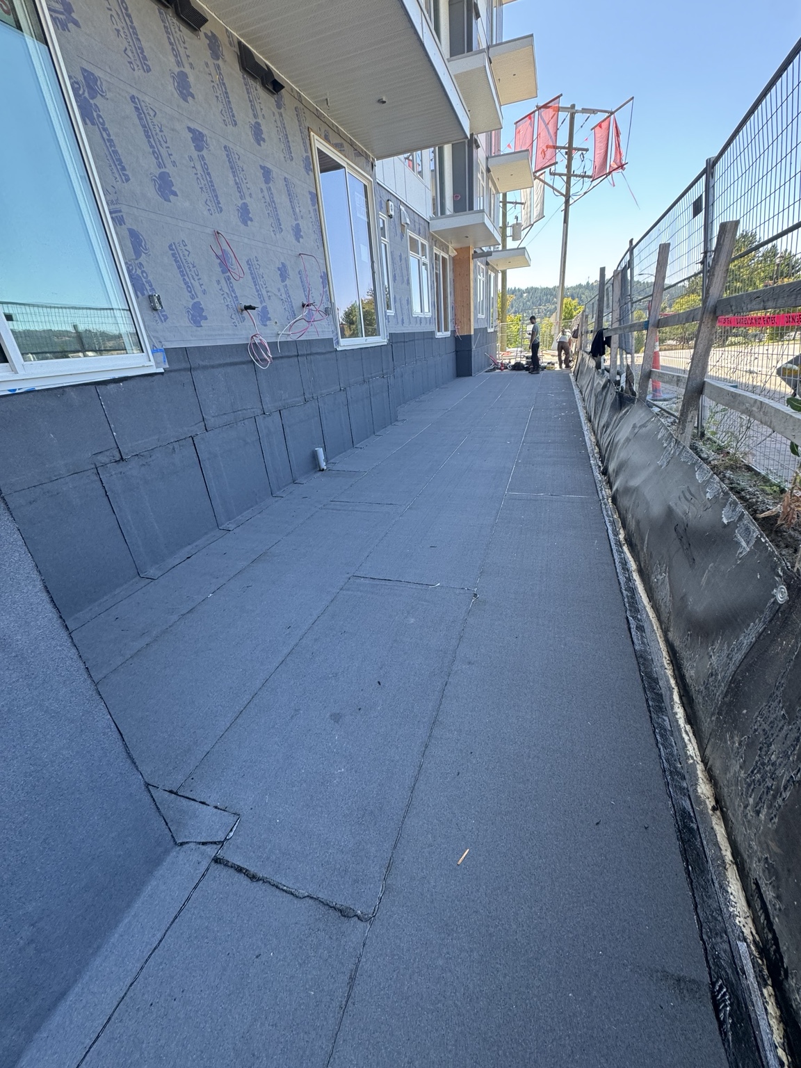 Membrane walkway along a building wall with upstands, windows and a fenced perimeter